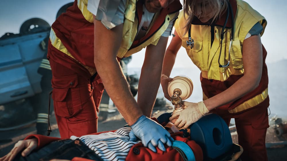 Paramedics assisting a female accident victim lying on a stretcher at a vehicle crash traffic accident scene.