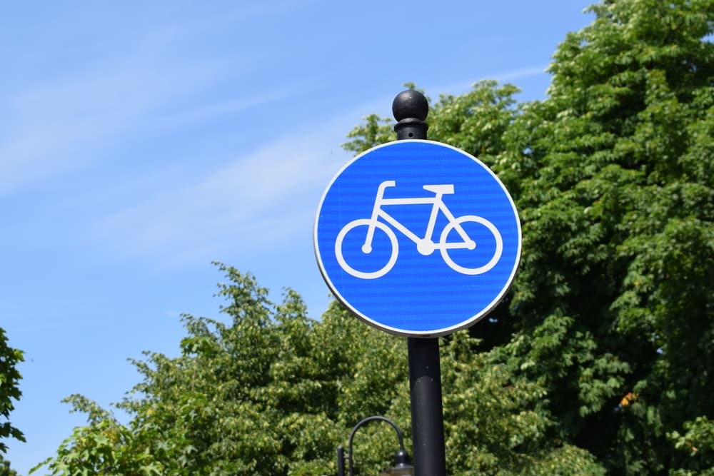 Bicycle sign in blue color with trees in the background, indicating a bike-friendly area or bike path.