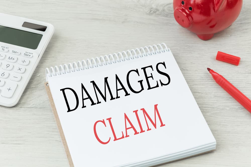 Damages claim text written on a notepad, placed on an office desk alongside a calculator and a red coin bank. Represents business insurance and personal claims