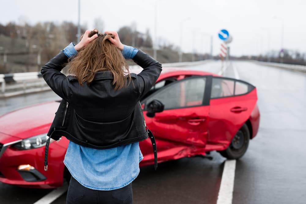 Woman stands near a sideswiped car after an accident.