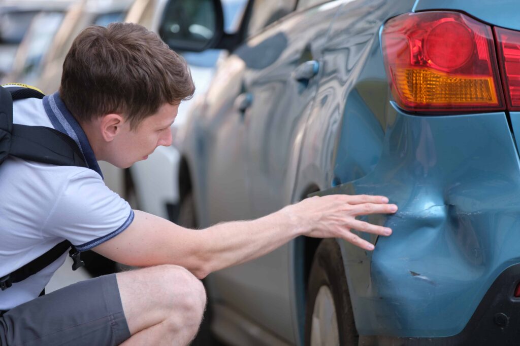 Man inspecting dented rear bumper of blue car after a minor collision.