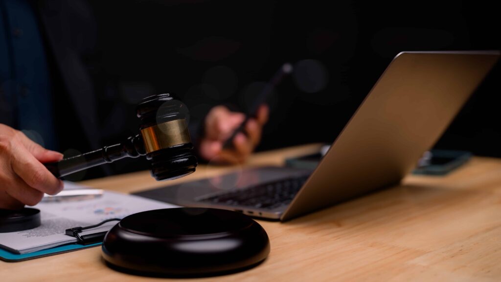 Judge holding gavel near laptop during an online court session or legal consultation. Judge holding gavel near laptop during an online court session or legal consultation.