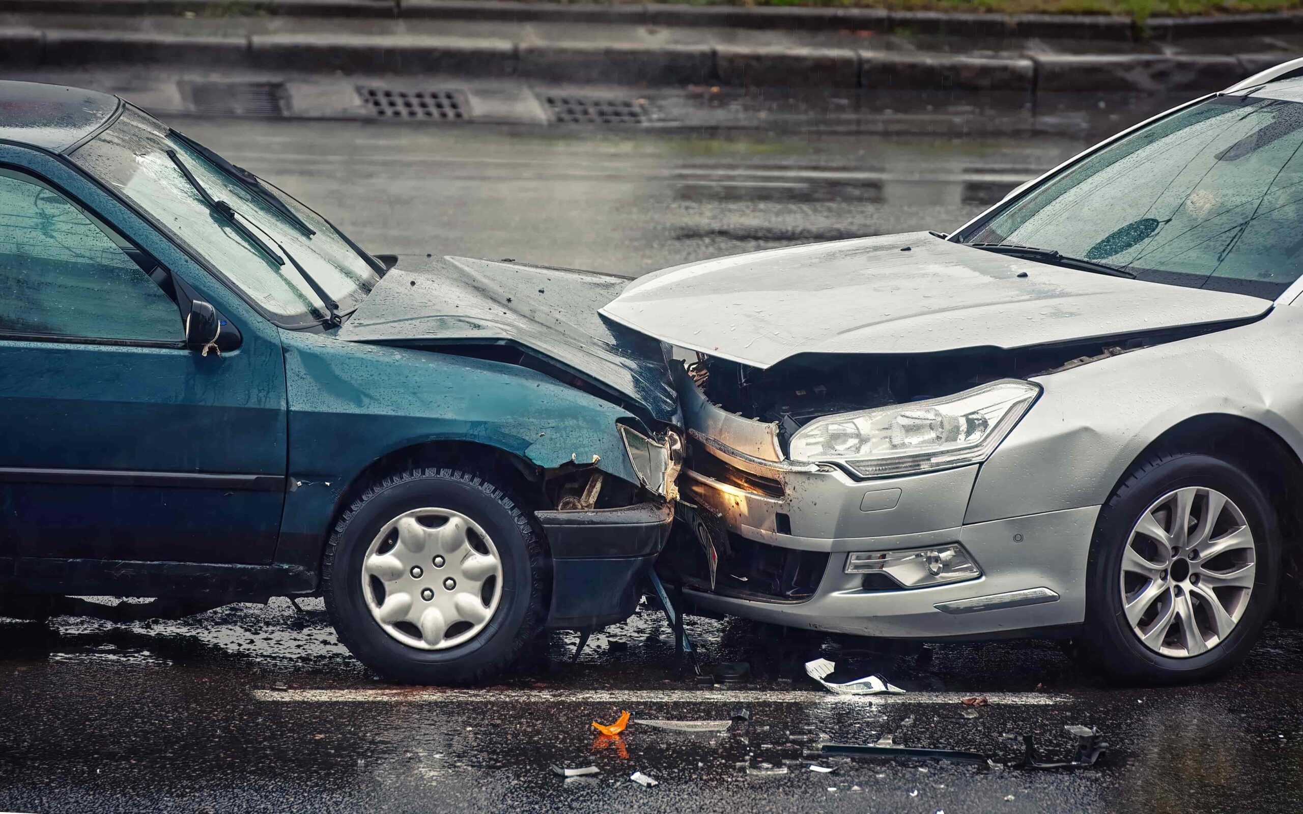 Two cars involved in a head-on collision on a wet road, showing front-end damage from a traffic accident.