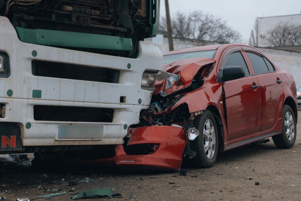 Severe front-end car crash with a red sedan collided into a large truck, showing extensive vehicle damage. Severe front-end car crash with a red sedan collided into a large truck, showing extensive vehicle damage.