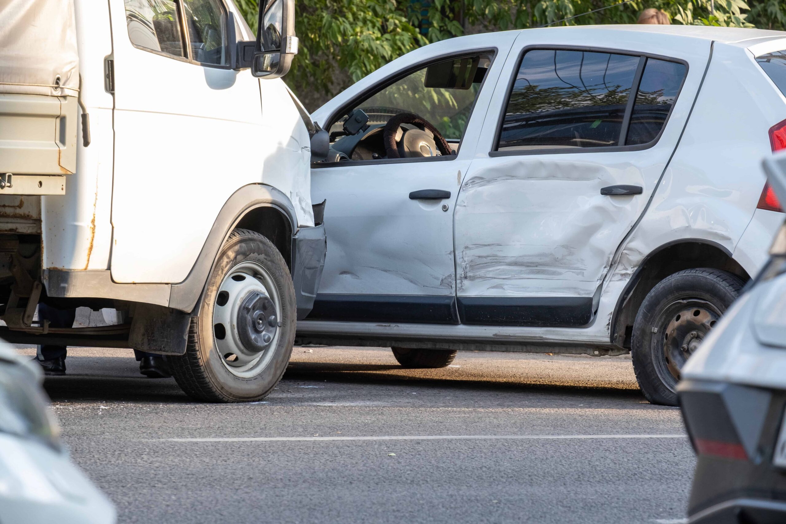 White passenger car with side damage after collision with a delivery truck in a traffic accident. White passenger car with side damage after collision with a delivery truck in a traffic accident.