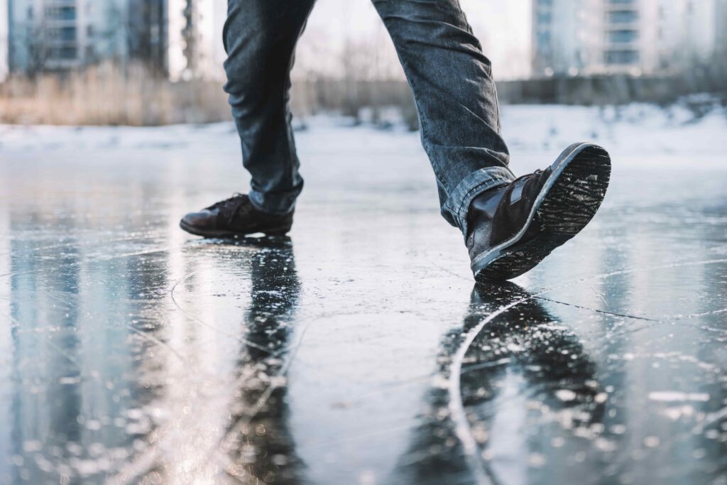 Person walking on icy sidewalk during winter, highlighting slip and fall accident risk.